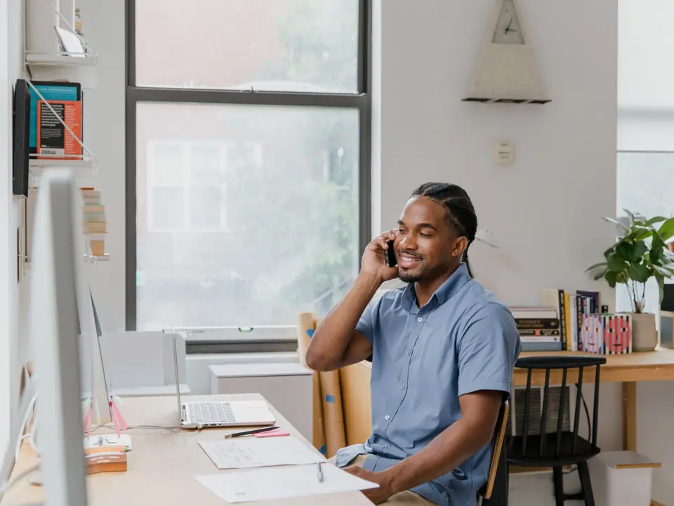 A smiling man on a phone call at a home-office desk